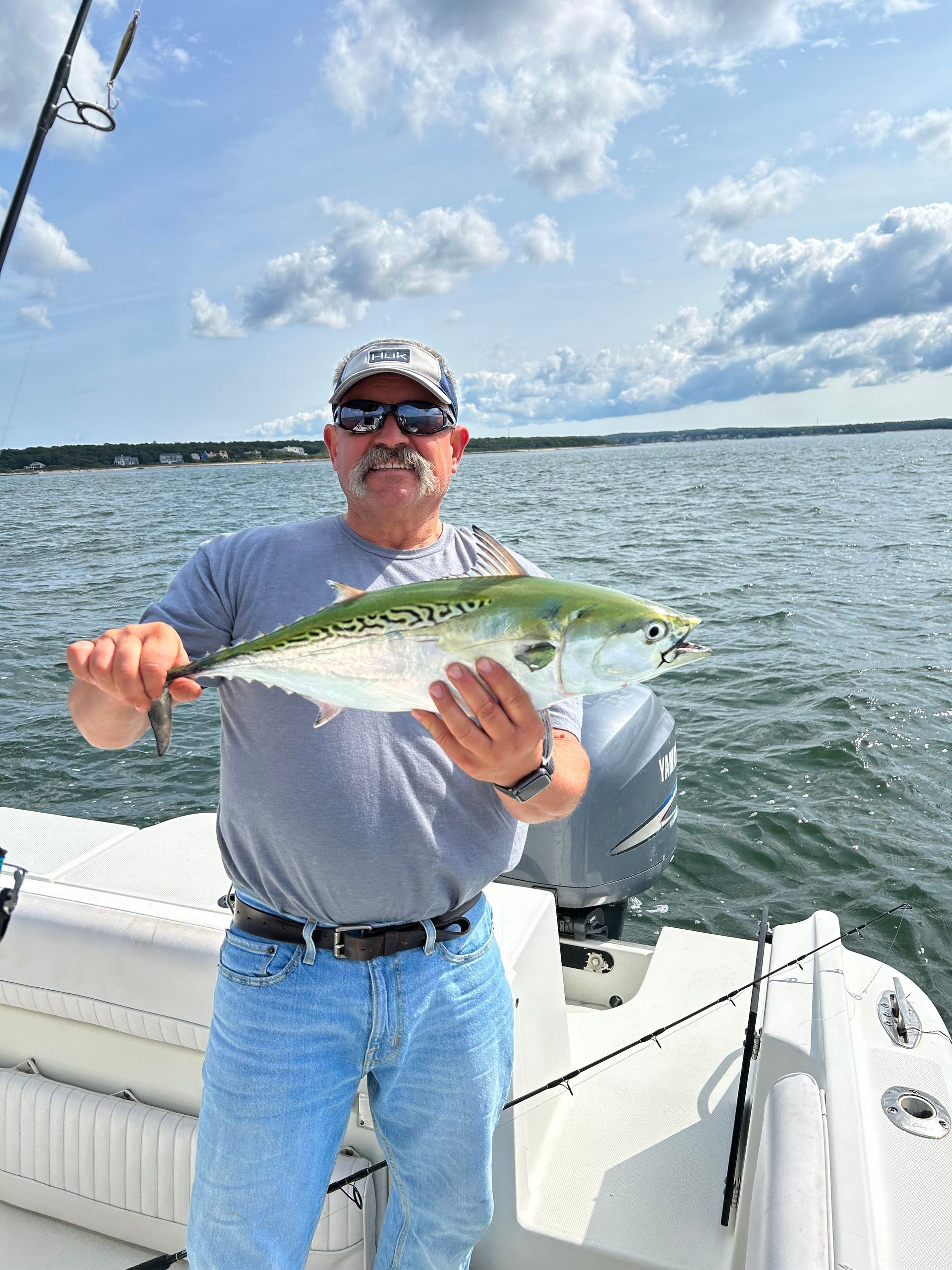 Man on a boat holding a fish he caught, water and sky in the background.