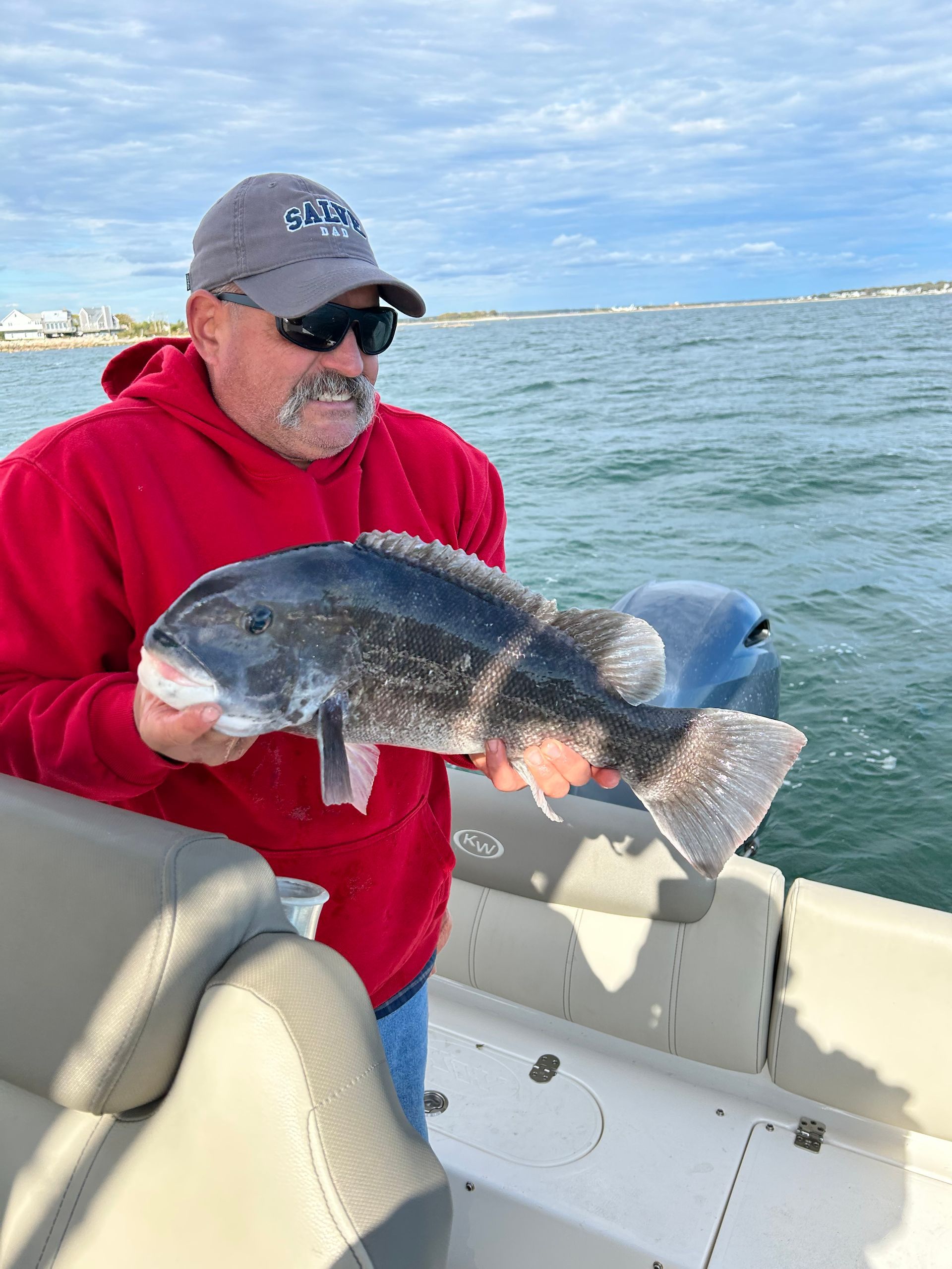 Man holding a large black fish on a boat; water and sky in the background.
