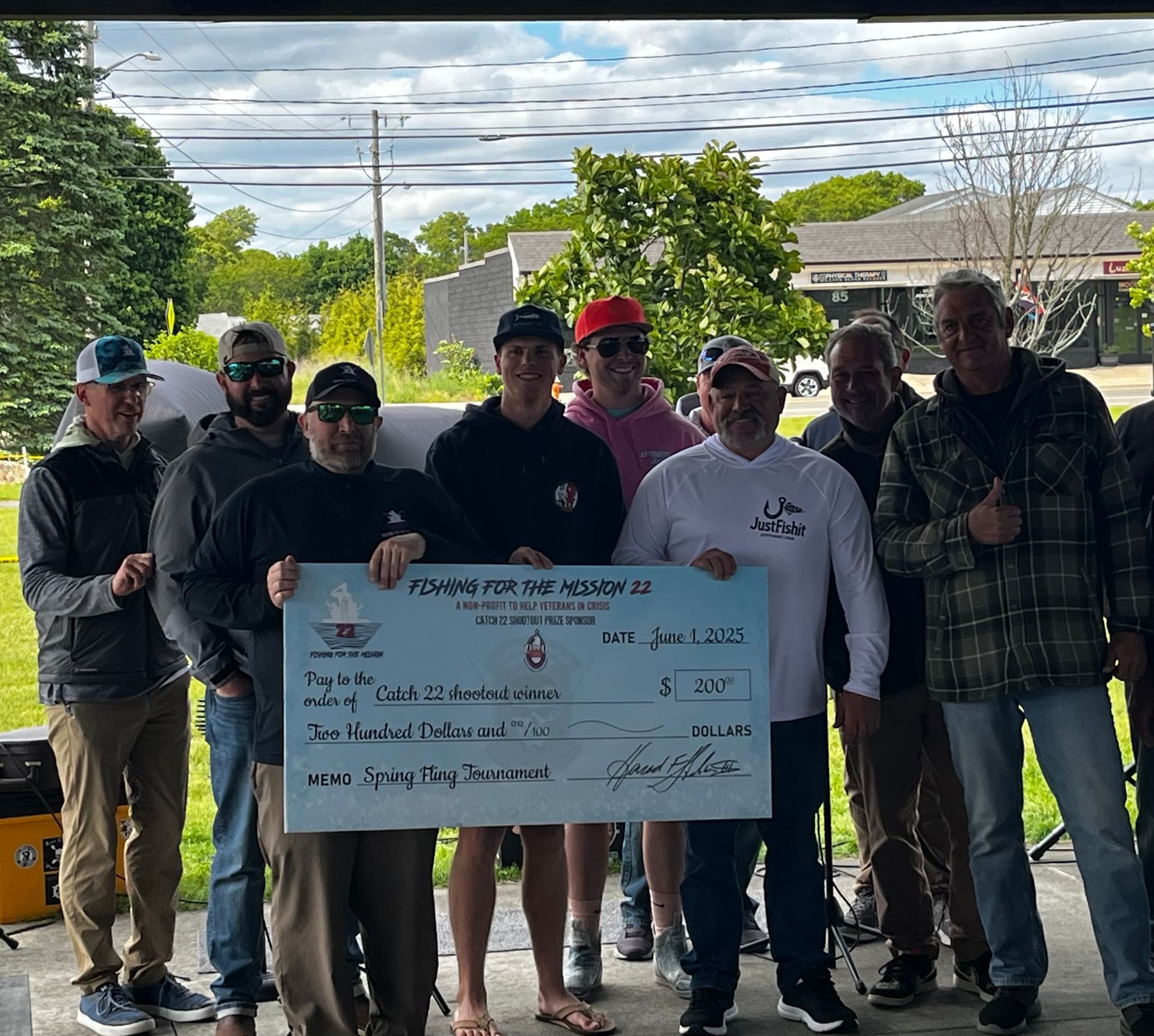 Group of men holding a large check outside, presumably an event donation.