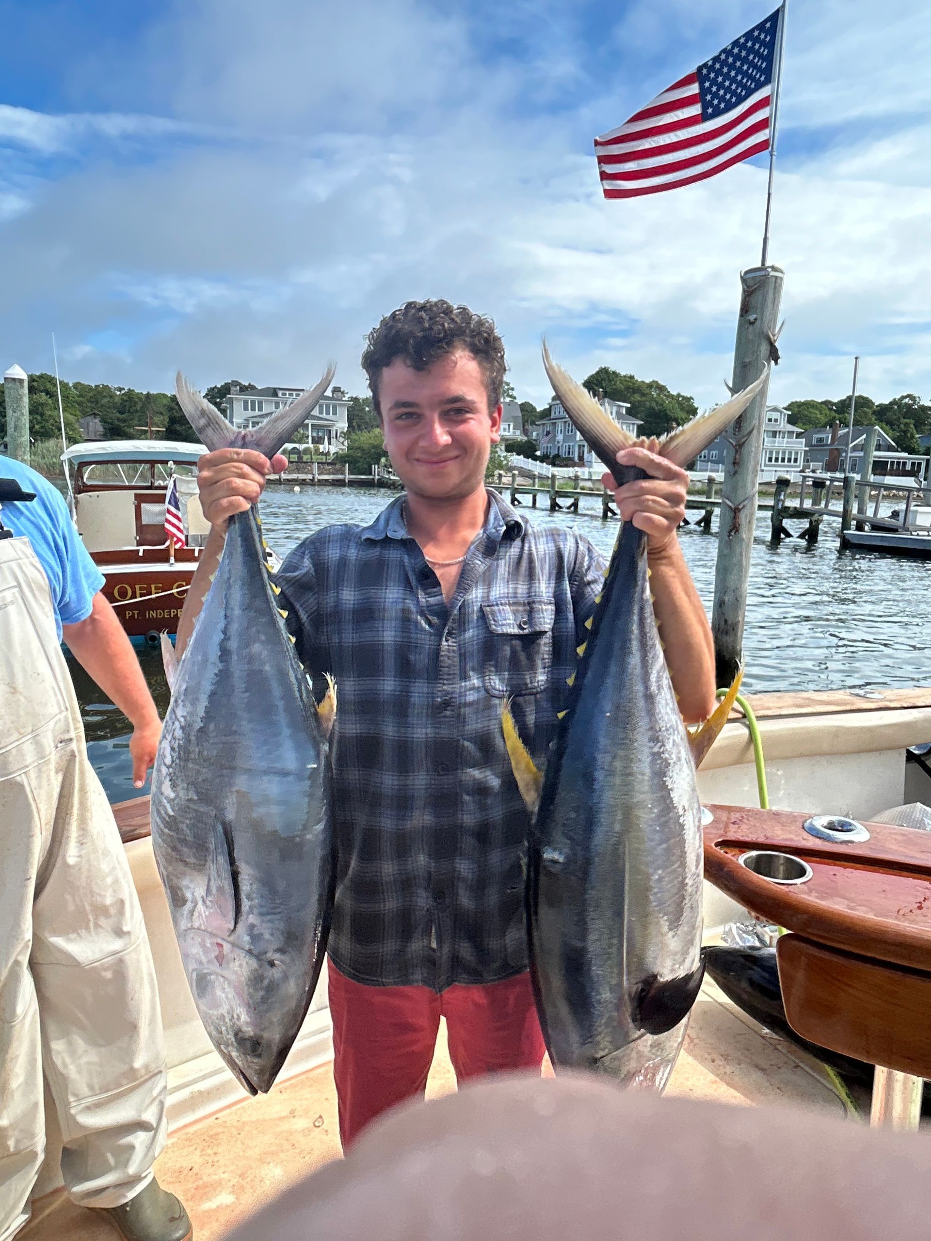 Man on boat holds up two large fish with US flag in background.