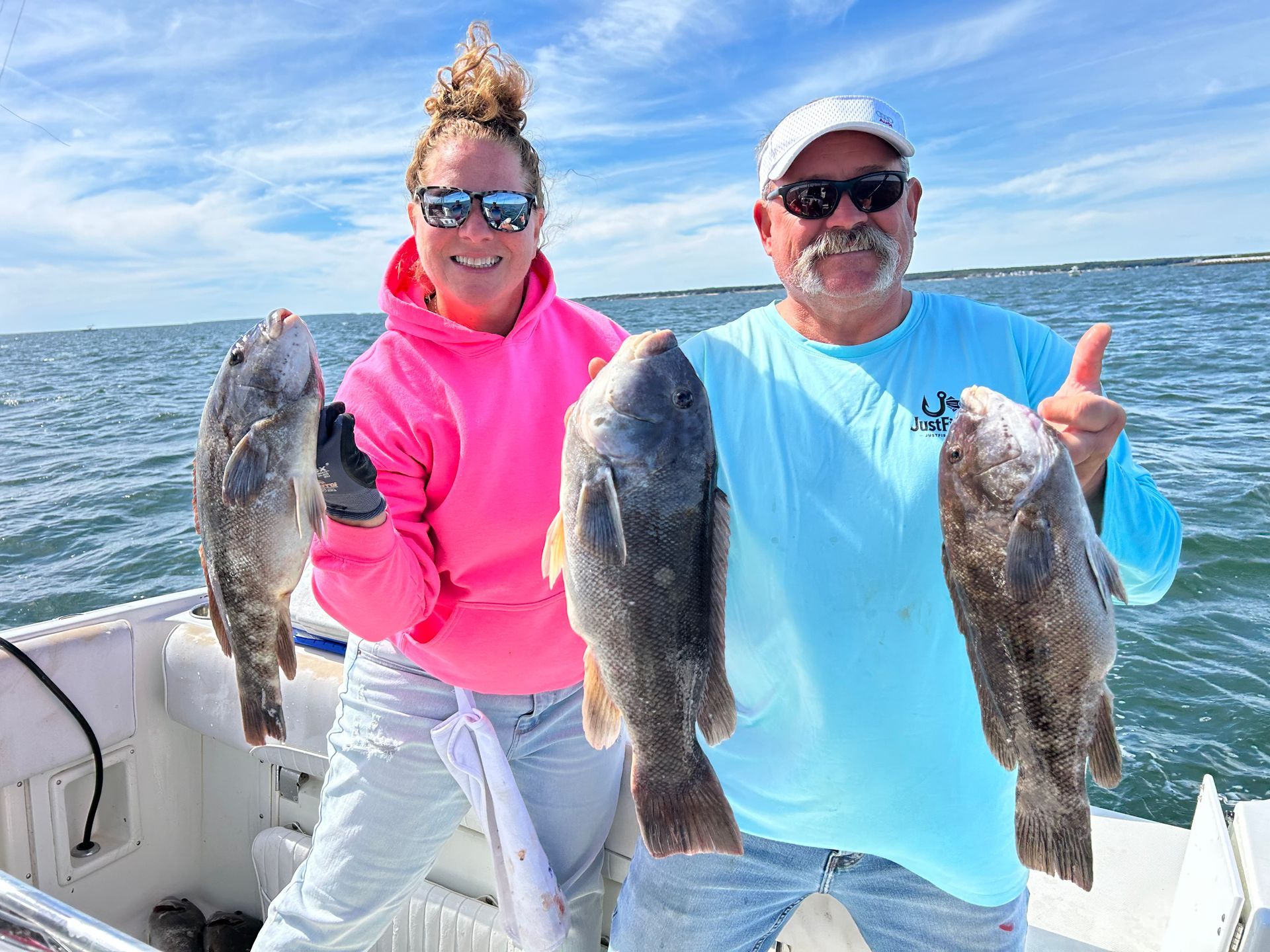 Two people on a boat display their caught fish, thumbs up, sunny day, blue water.