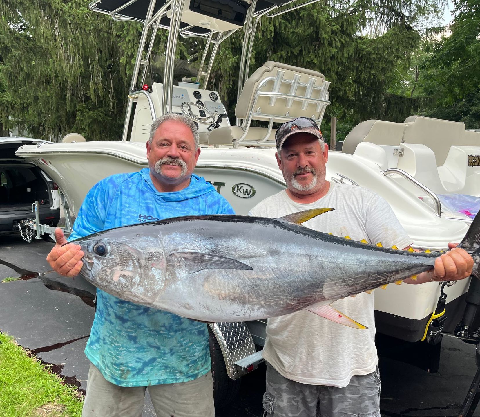 Two men hold a large yellowfin tuna in front of a boat.