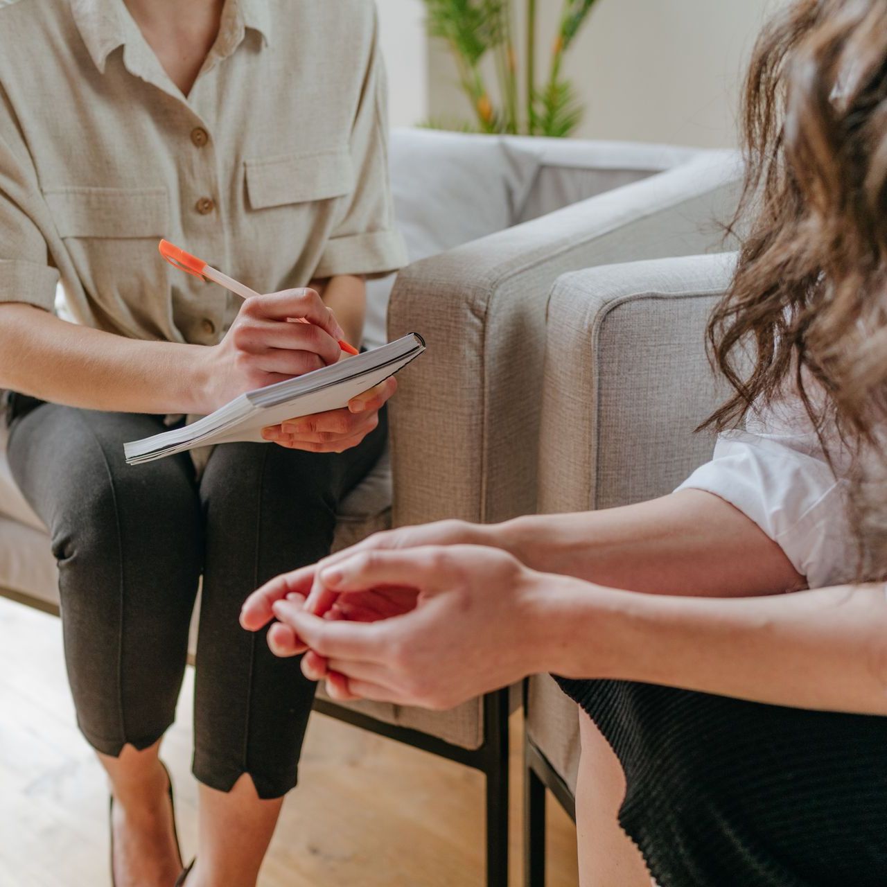 A woman is sitting in a chair talking to another woman who is writing in a notebook.