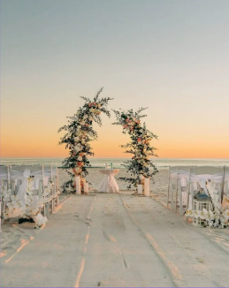 Decoração de casamento na praia com arco floral ao pôr do sol.
