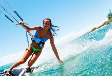 Mulher praticando kitesurf nas águas azuis do oceano, sorrindo sob a luz do sol.