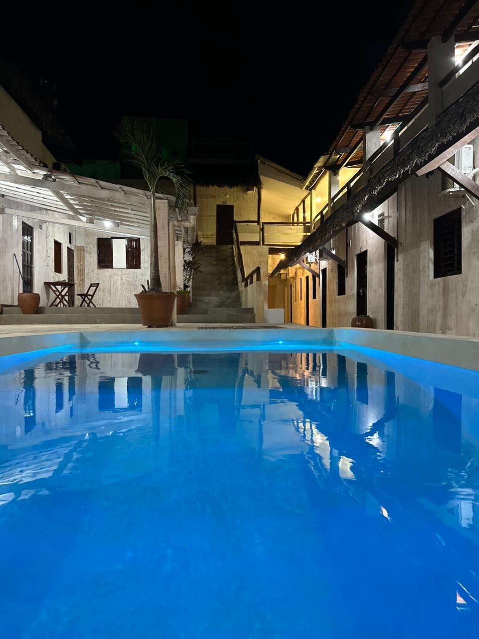 Vista noturna de uma piscina iluminada em azul num pátio com edifícios.