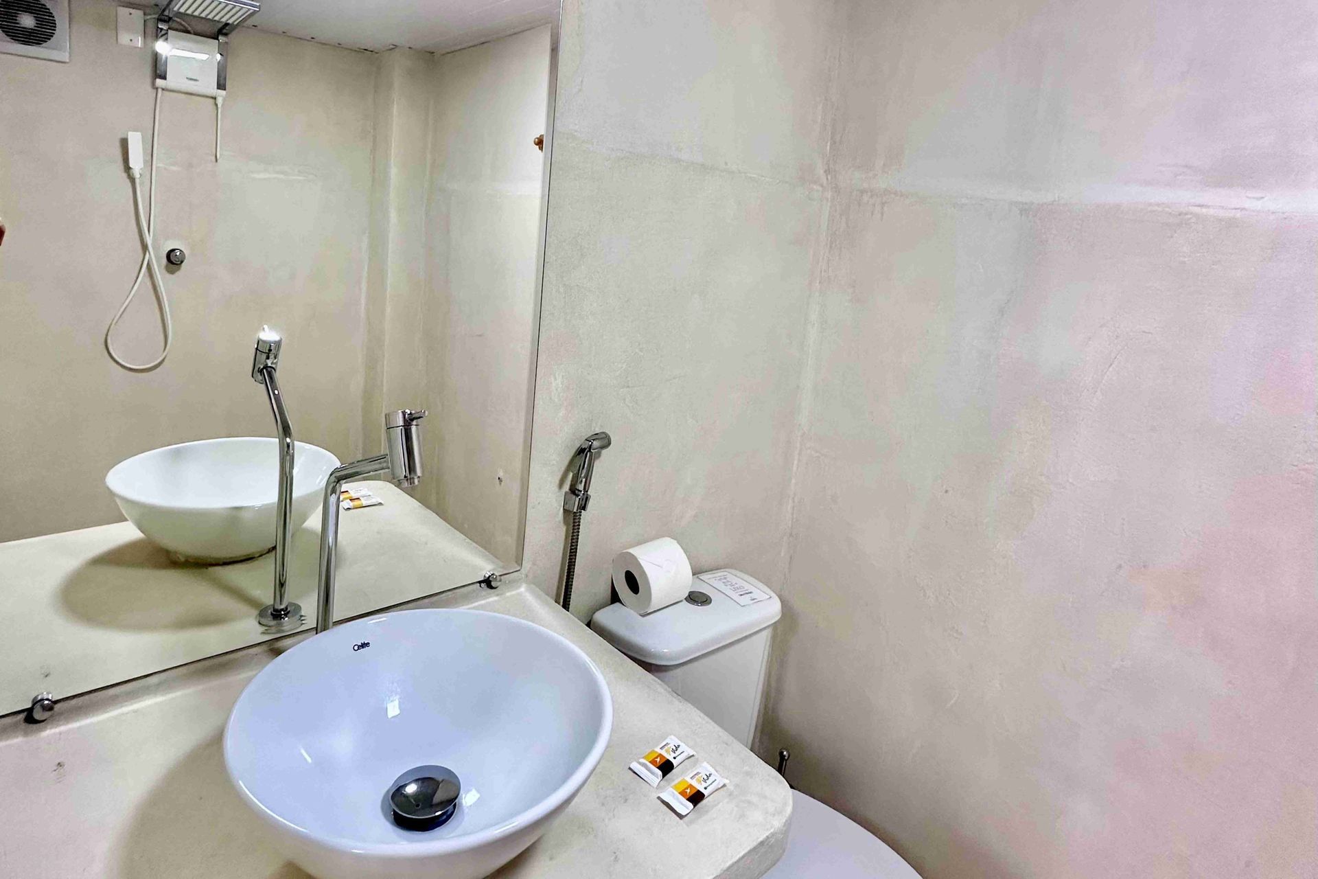 Banheiro pequeno com pia, vaso sanitário e espelho brancos. Paredes brancas.