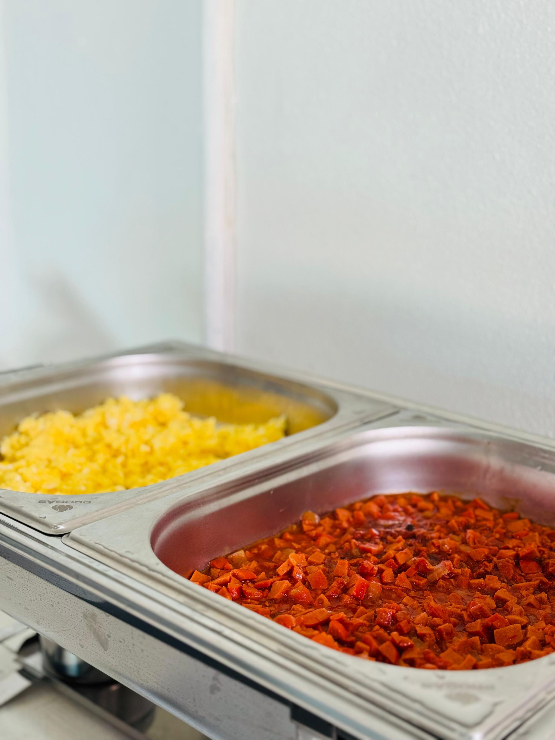 Um aquecedor de alimentos de metal com ovos mexidos amarelos e ensopado vermelho à base de tomate.