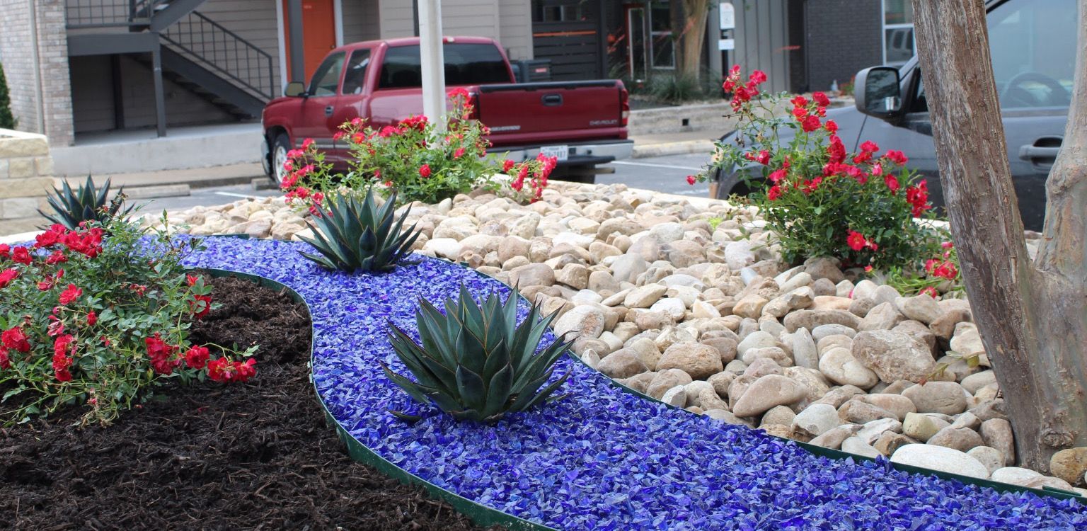 A red truck is parked in front of a garden with blue gravel and flowers.