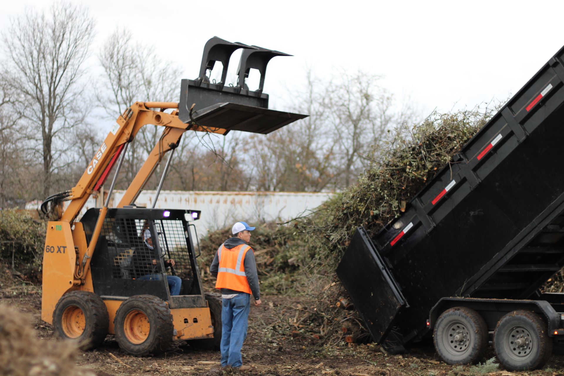 A man in an orange vest is standing next to a dump truck.
