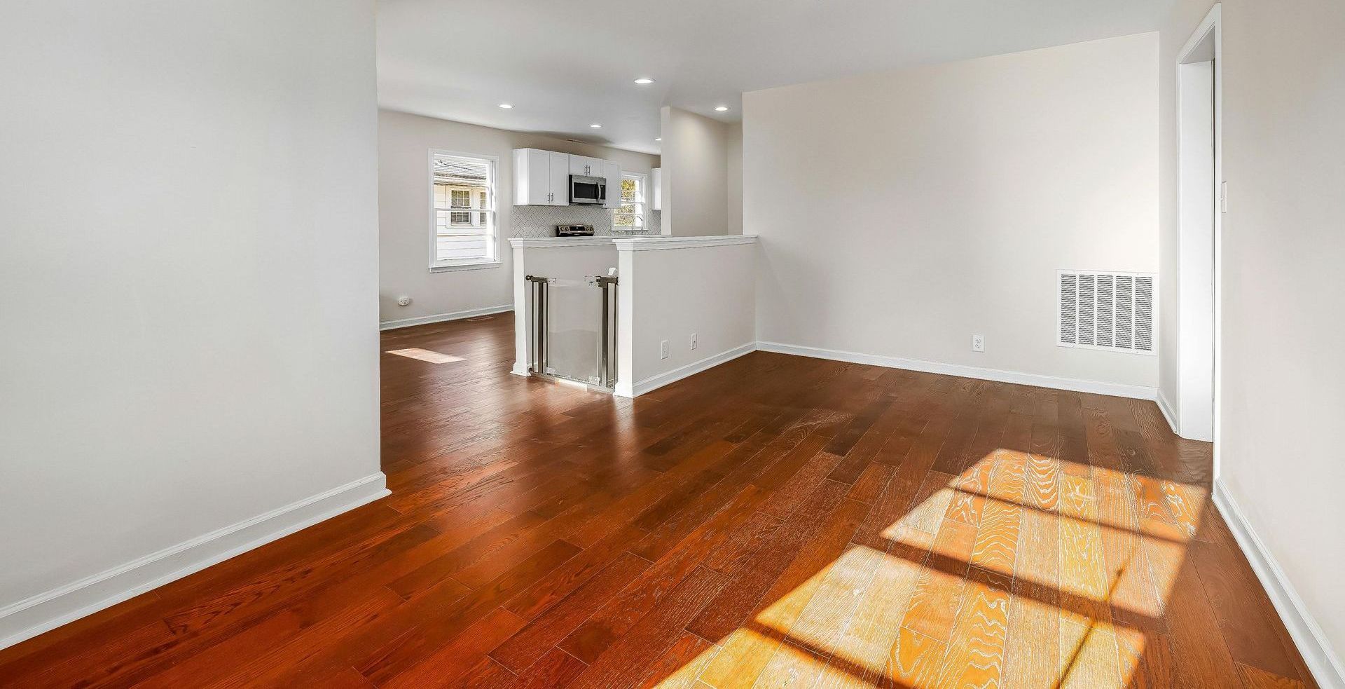 An empty living room with hardwood floors and white walls.