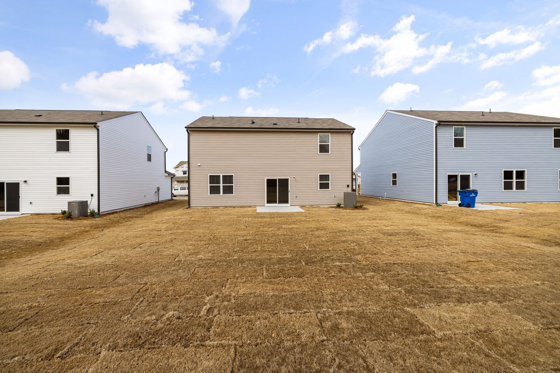Three beige and white houses in a row on a grassy lot under a partly cloudy sky.