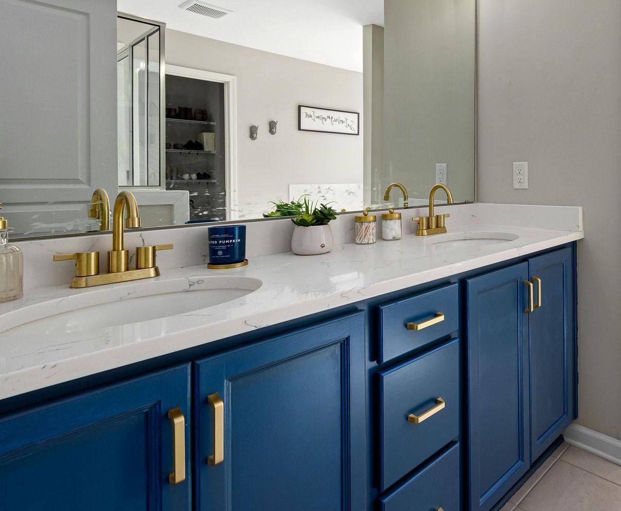A bathroom with two sinks , a mirror and blue cabinets.