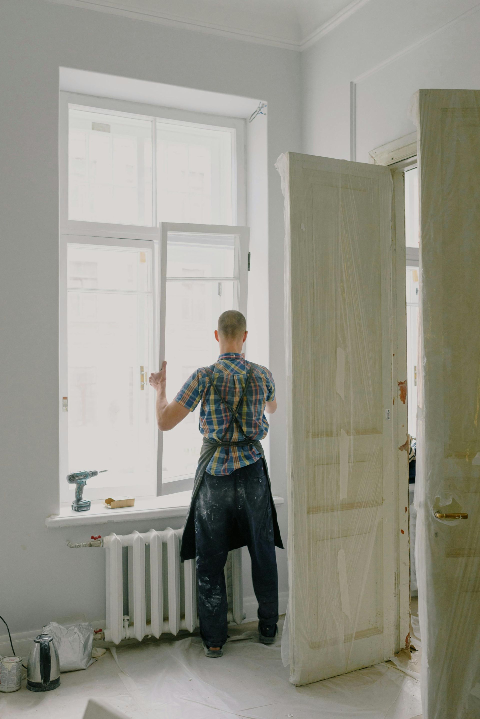 A man is standing in a room looking out of a window.