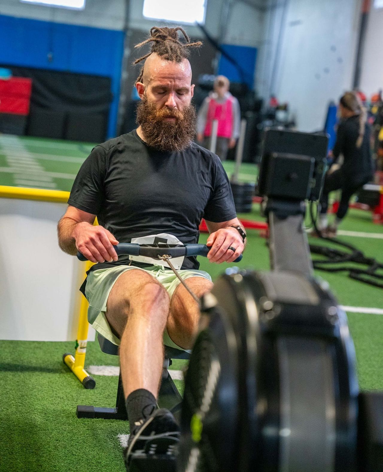 A man with a beard is rowing a machine during a HYROX Conditioning Class at Olympia Performance gym in Montreal