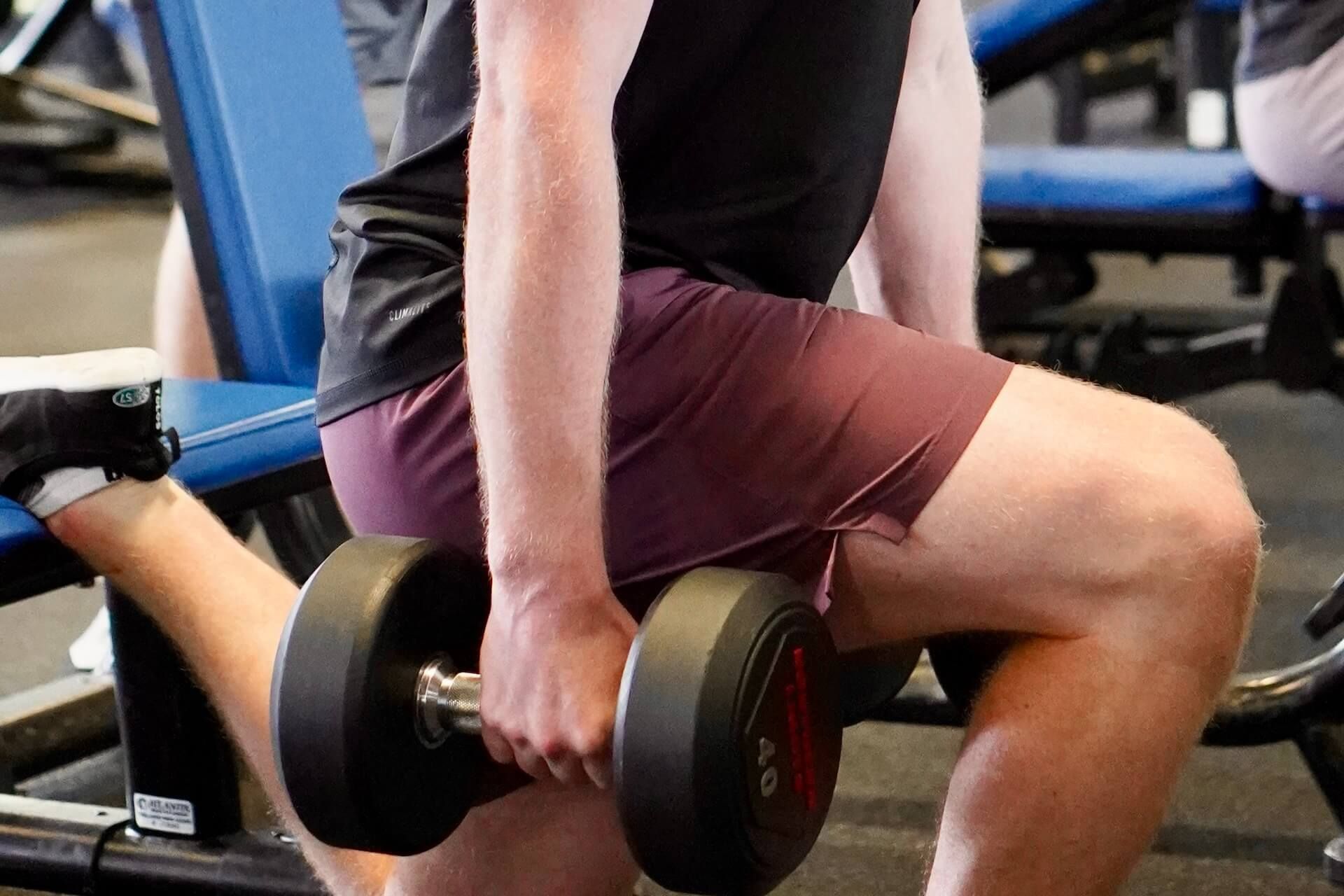 A man is sitting on a bench in a gym holding a dumbbell.