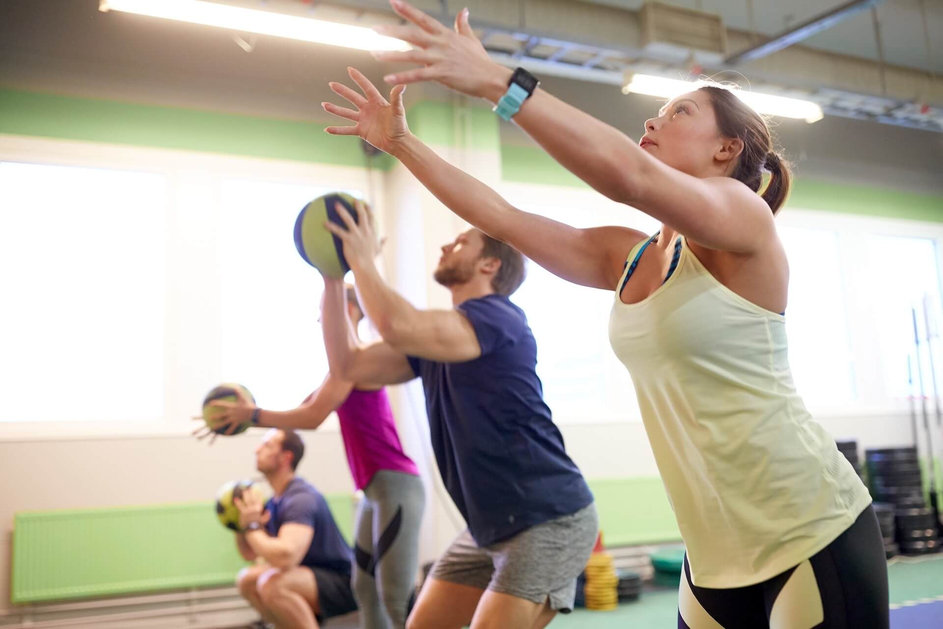 People exercising with medicine balls in a gym, woman reaching upward.