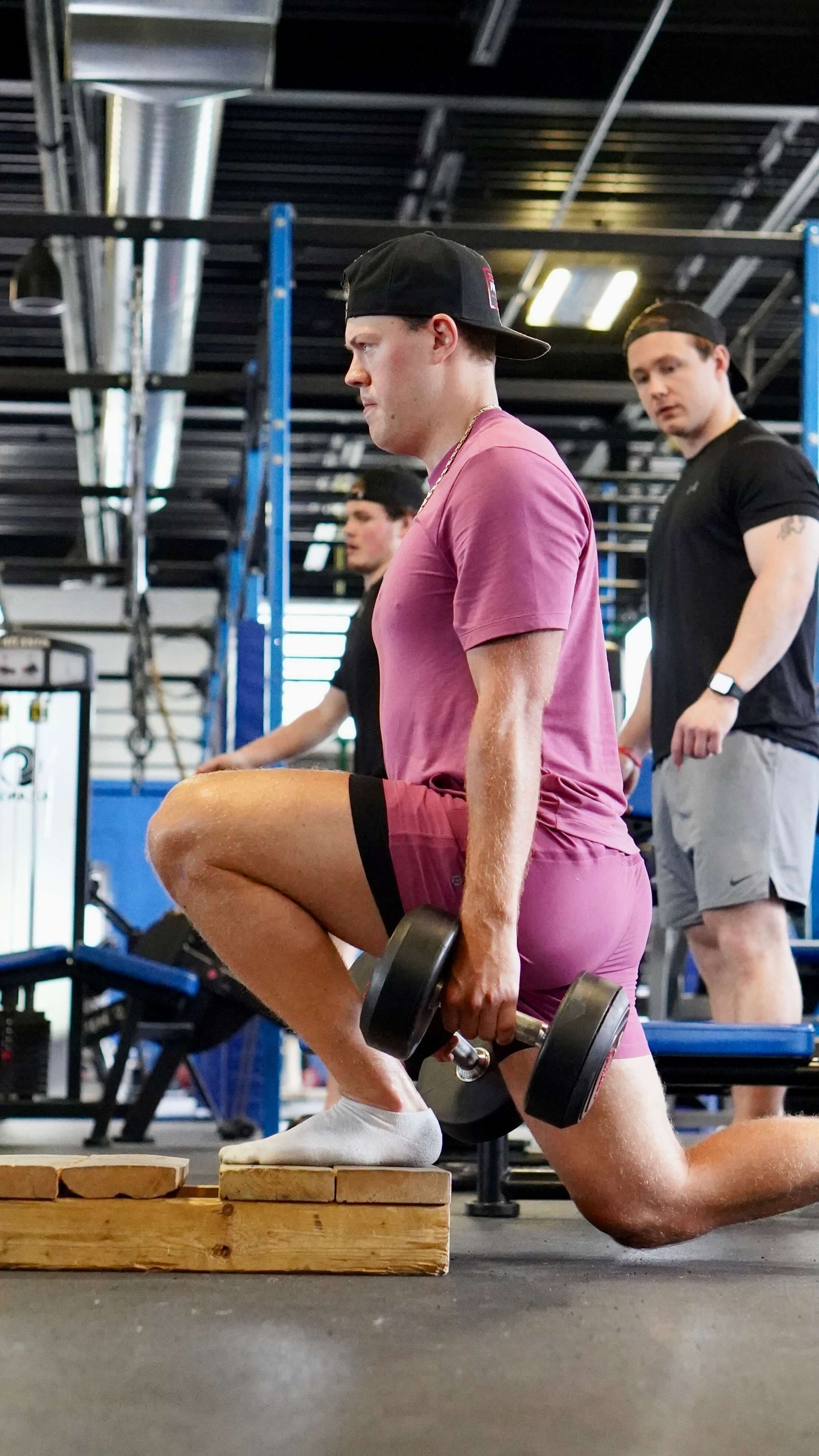 A man is squatting down while holding a dumbbell in a gym.