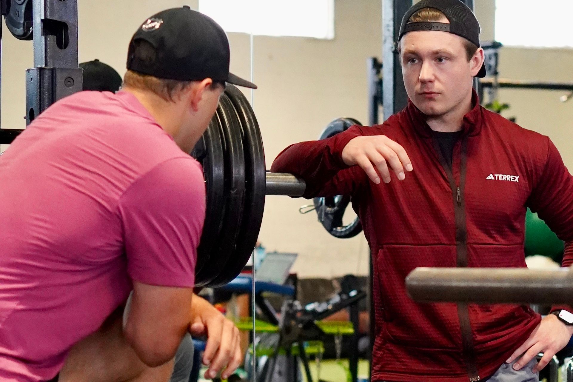 Two men are squatting down in a gym and talking to each other.