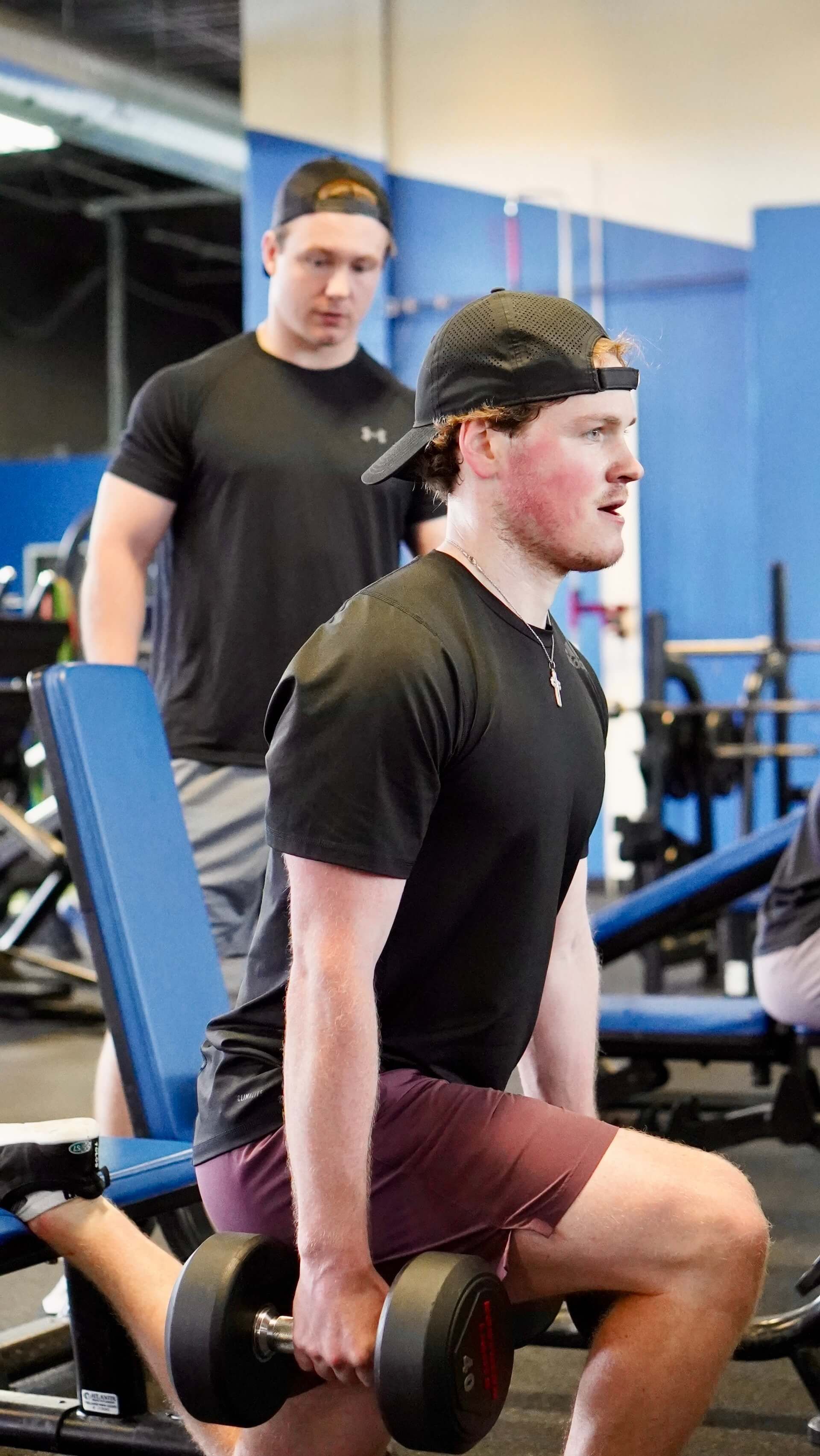 A man is squatting with a dumbbell in a gym.