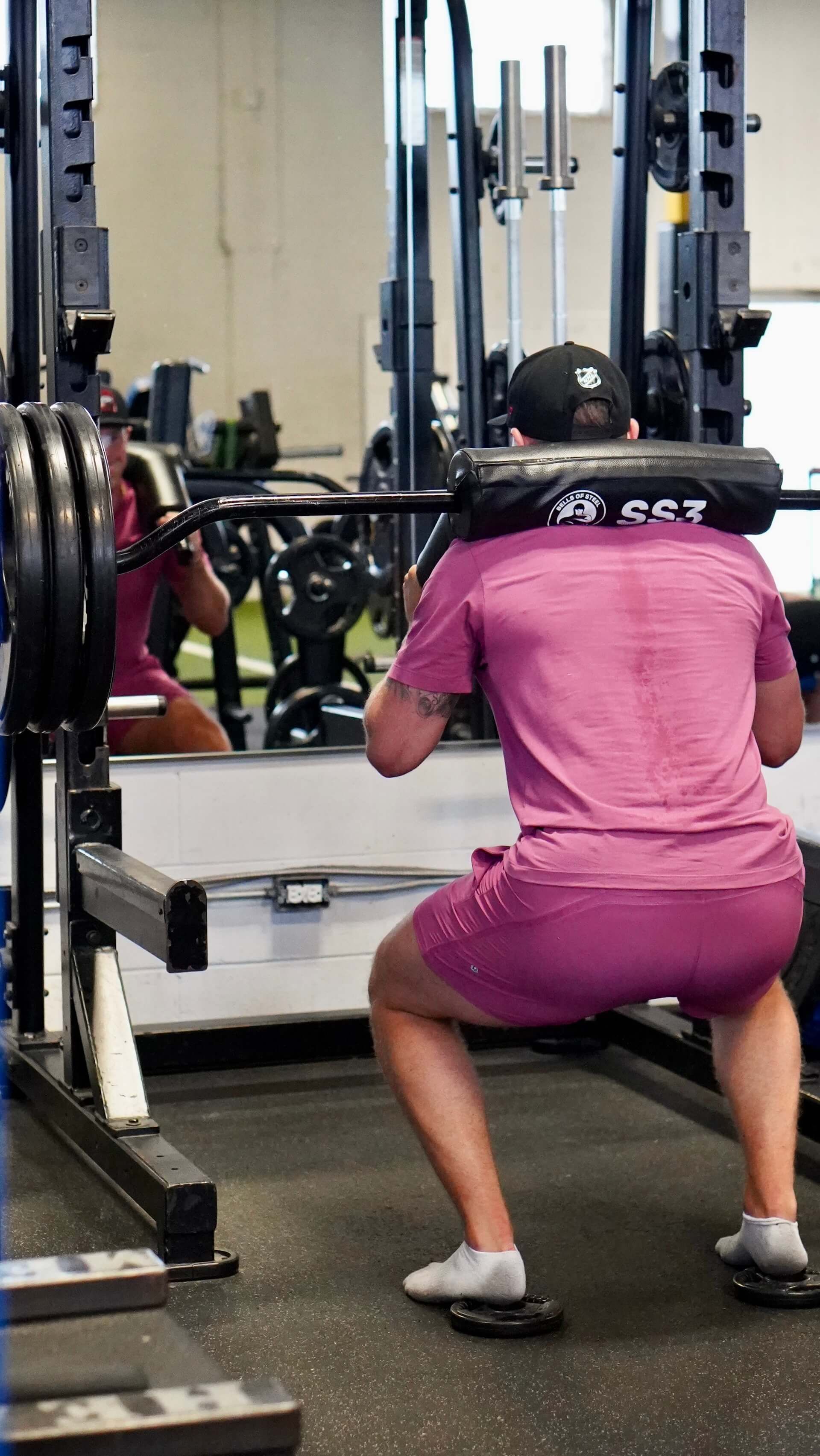 A woman in a pink shirt is squatting with a barbell in a gym.