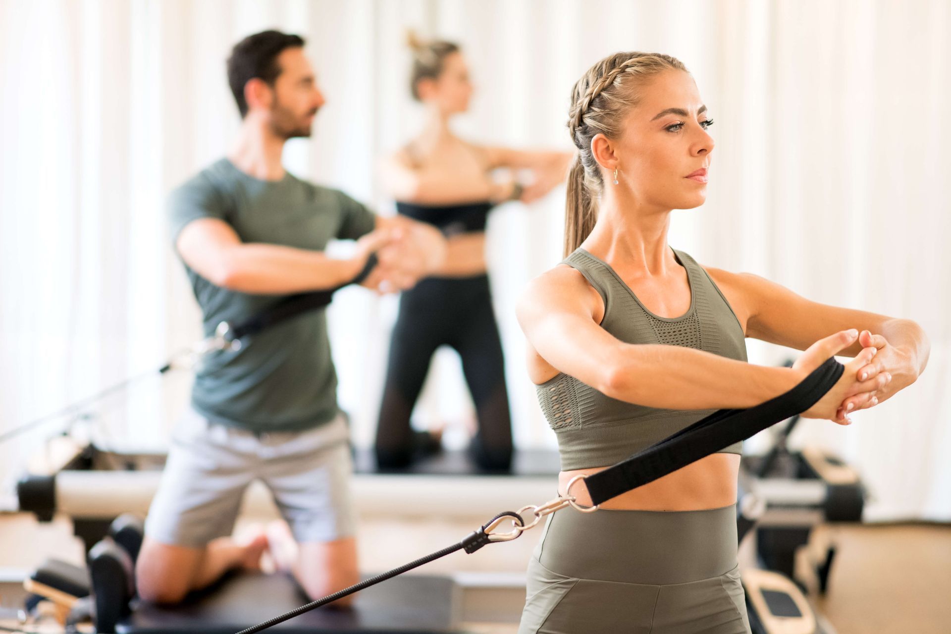 People doing Pilates, using equipment, in a light-filled studio, focused expressions.