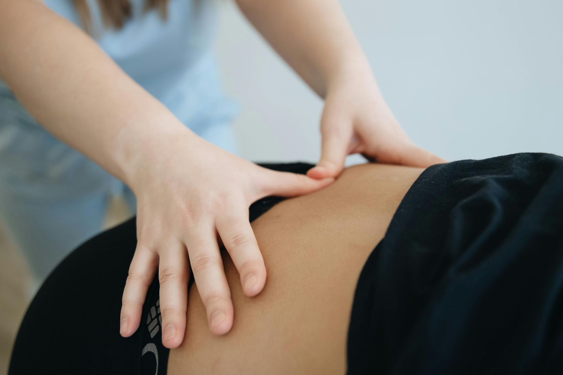 A practitioner performs a therapeutic massage on the lower back of a person wearing black clothing.