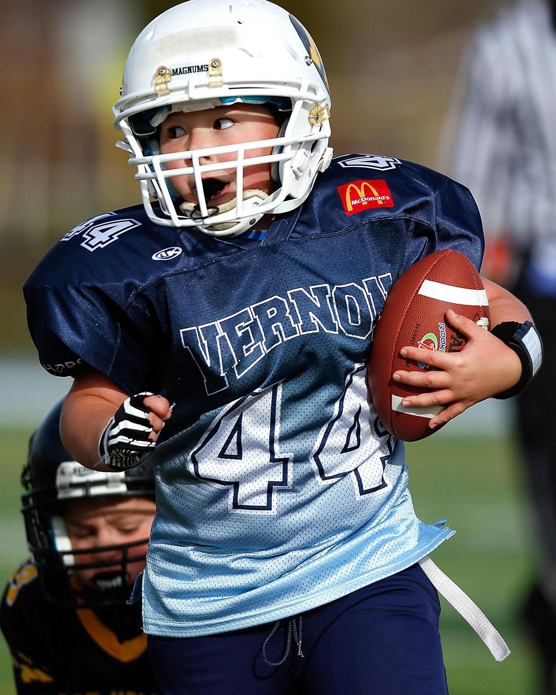 Boy in football uniform running with the ball; helmet, blue jersey with 