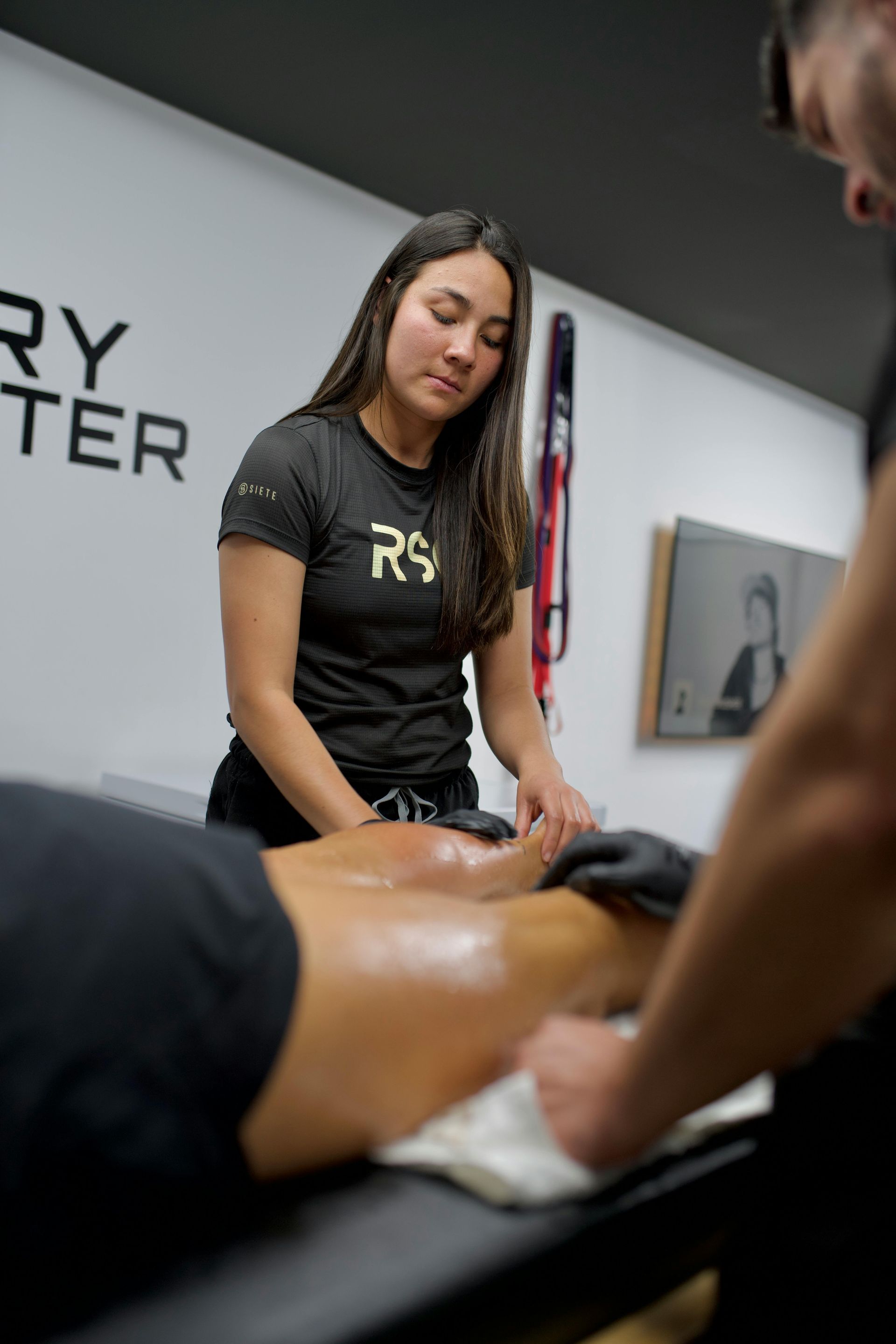 A professional masseuse performs a leg massage on a client lying on a table in a clinic setting.