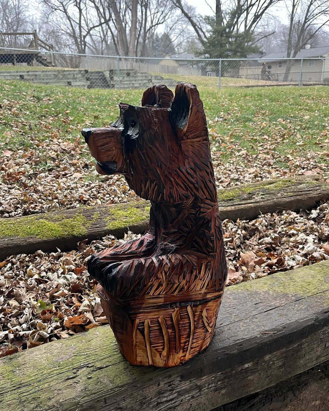 A wooden statue of a bear is sitting on a wooden ledge.