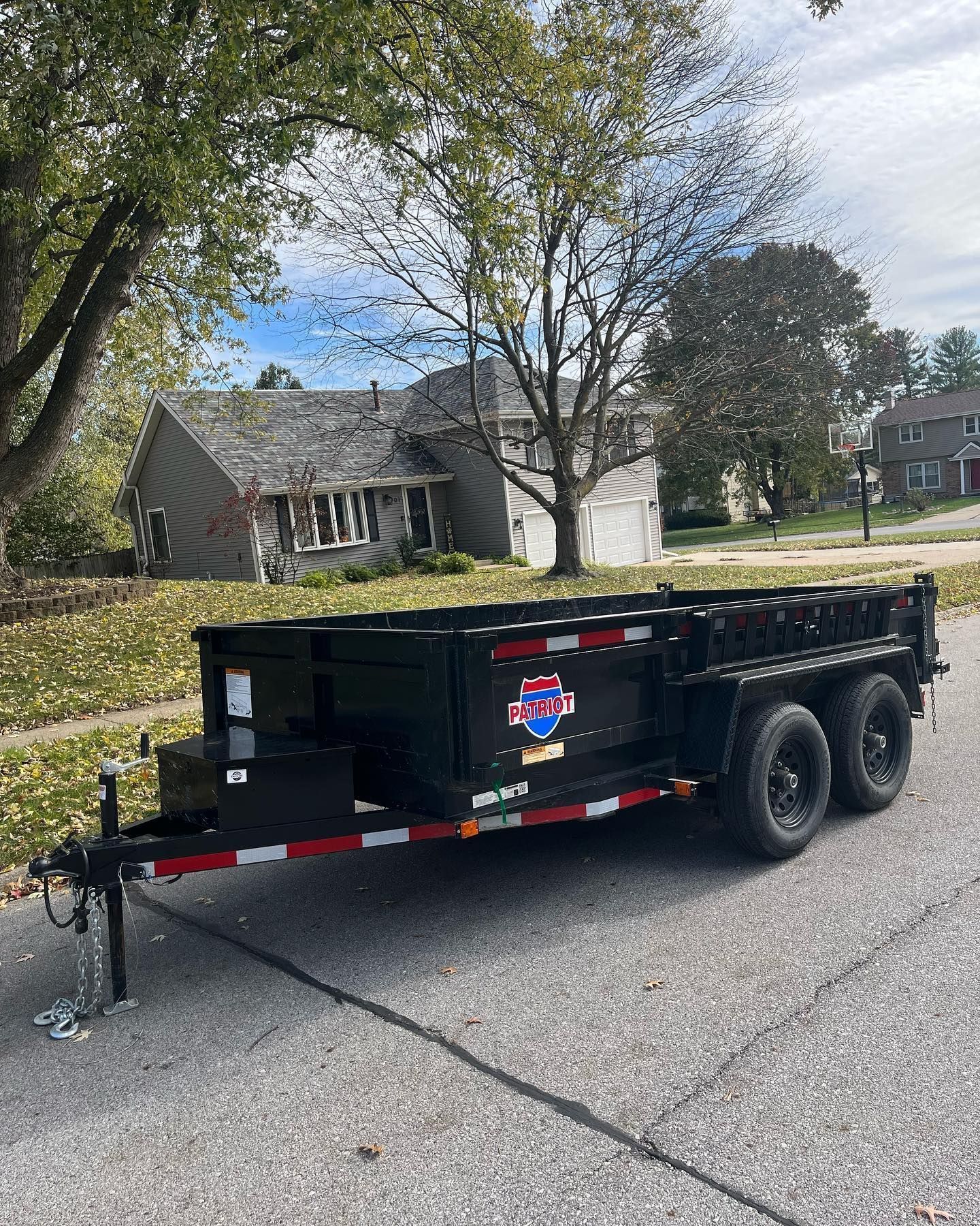 A dump trailer is parked on the side of the road in front of a house.