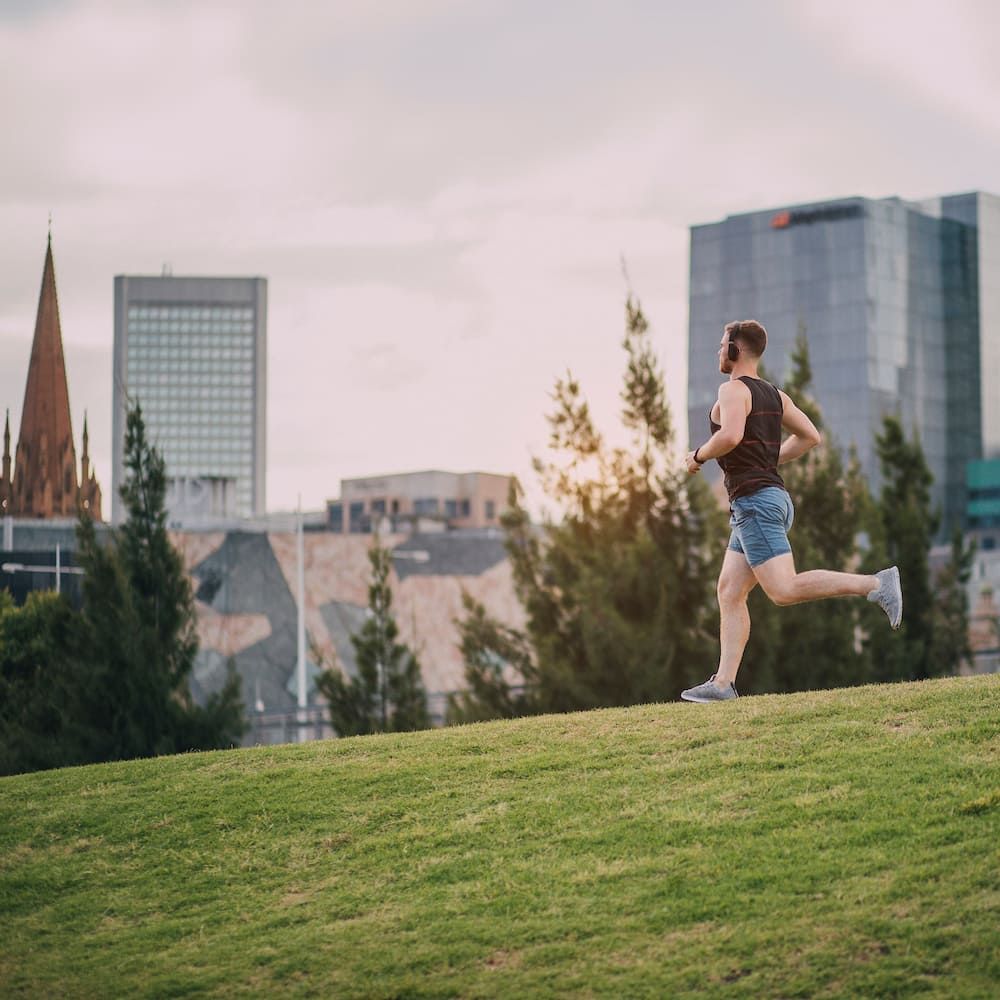 A Woman Is Running On A Grassy Hill In Front Of A City Skyline — Sea & Sand Chiropractic In Toukley, NSW