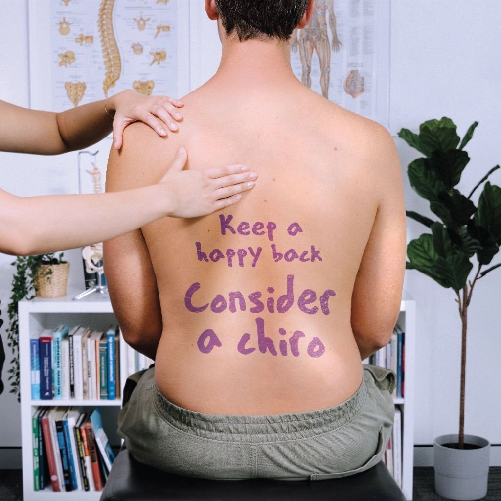 A Man Is Sitting On A Table With Writing On His Back — Sea & Sand Chiropractic In Toukley, NSW