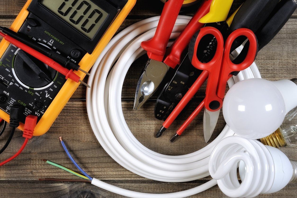 Multímetro y herramientas eléctricas con alambre enrollado, tijeras, bombillas y cables sobre un banco de trabajo.
