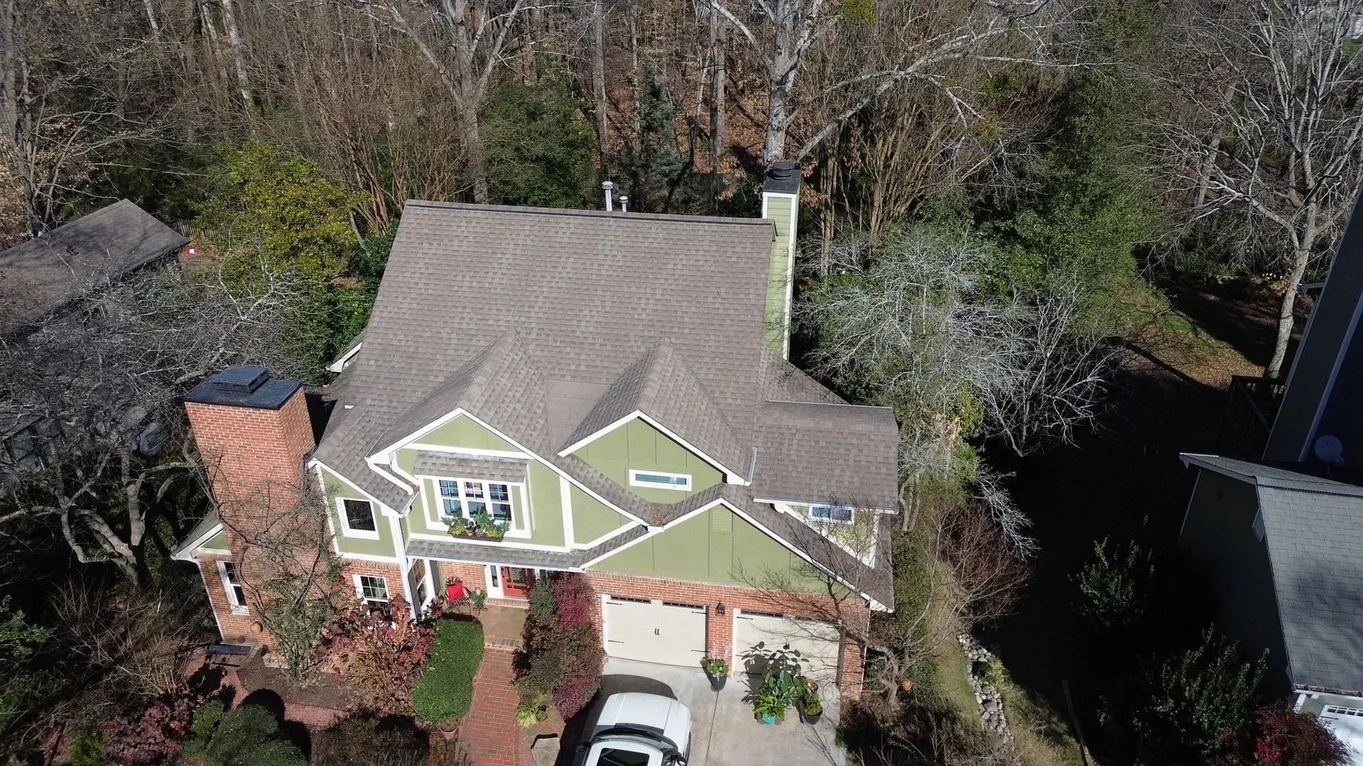 An aerial view of a large house with a car parked in front of it surrounded by trees.