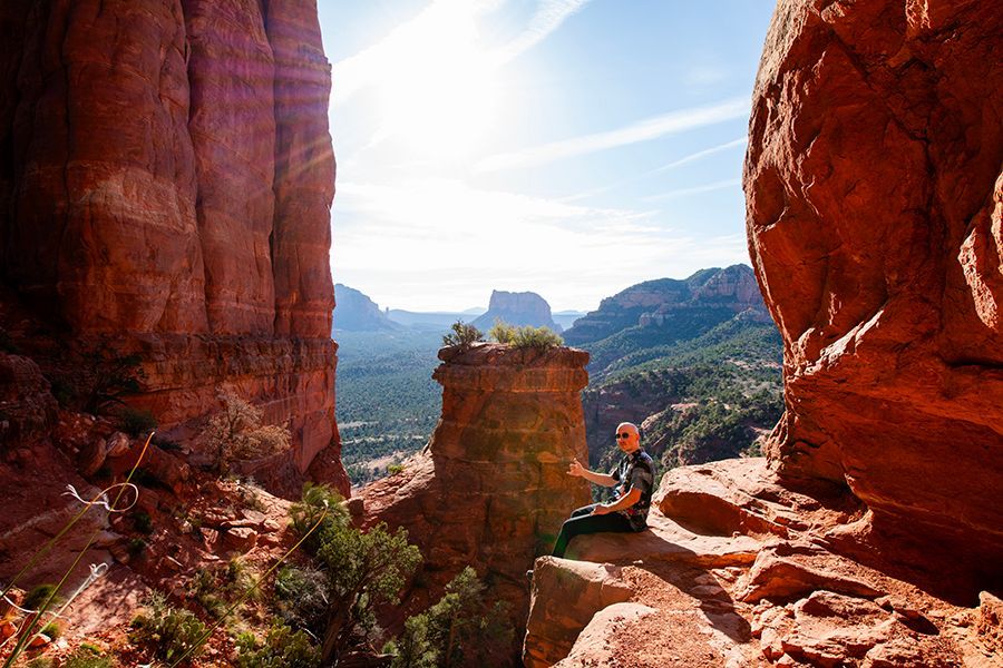 Person meditating on a red rock formation, canyon view. Sunny day.