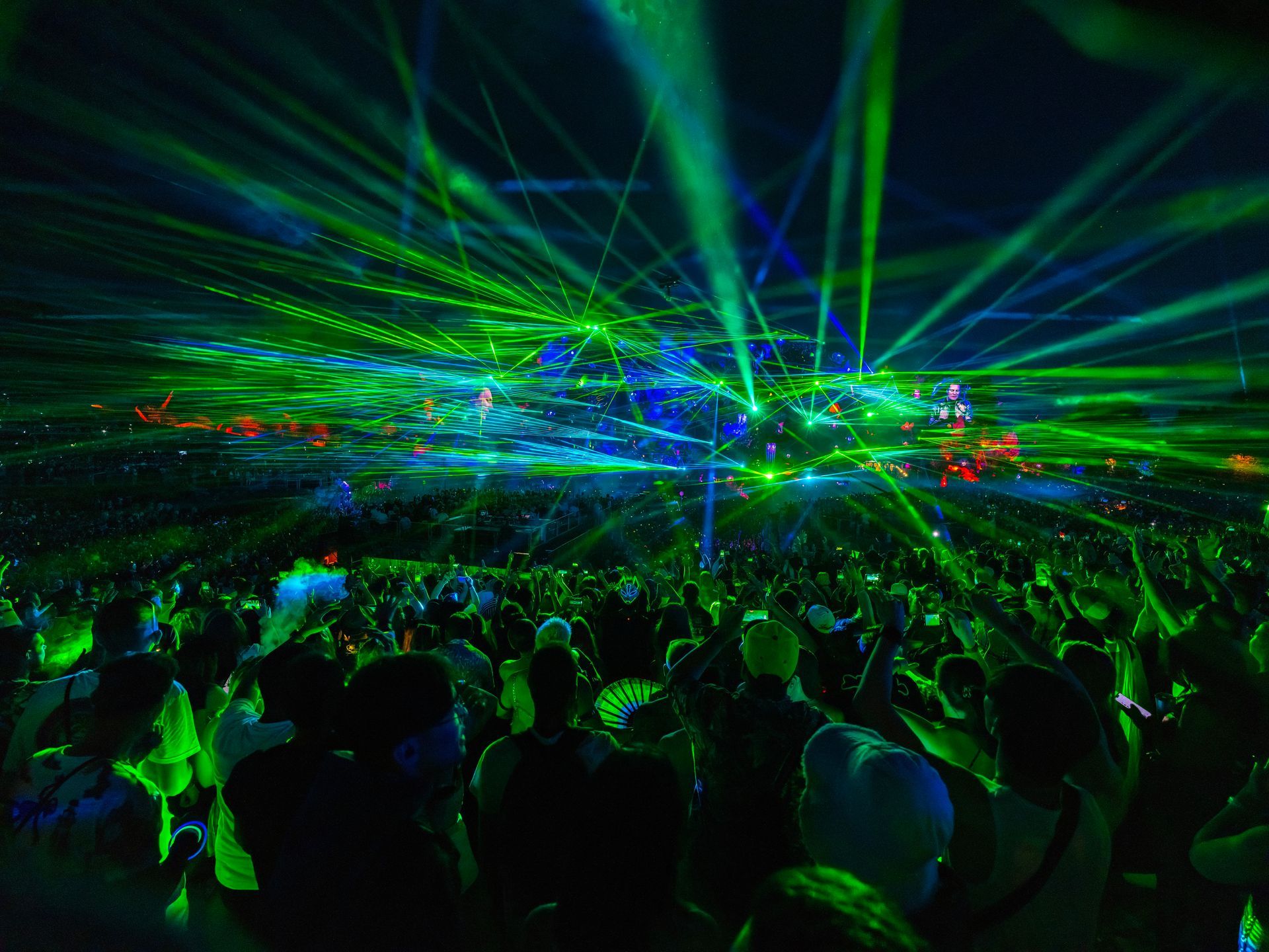 Crowd at a concert under green and blue laser lights.