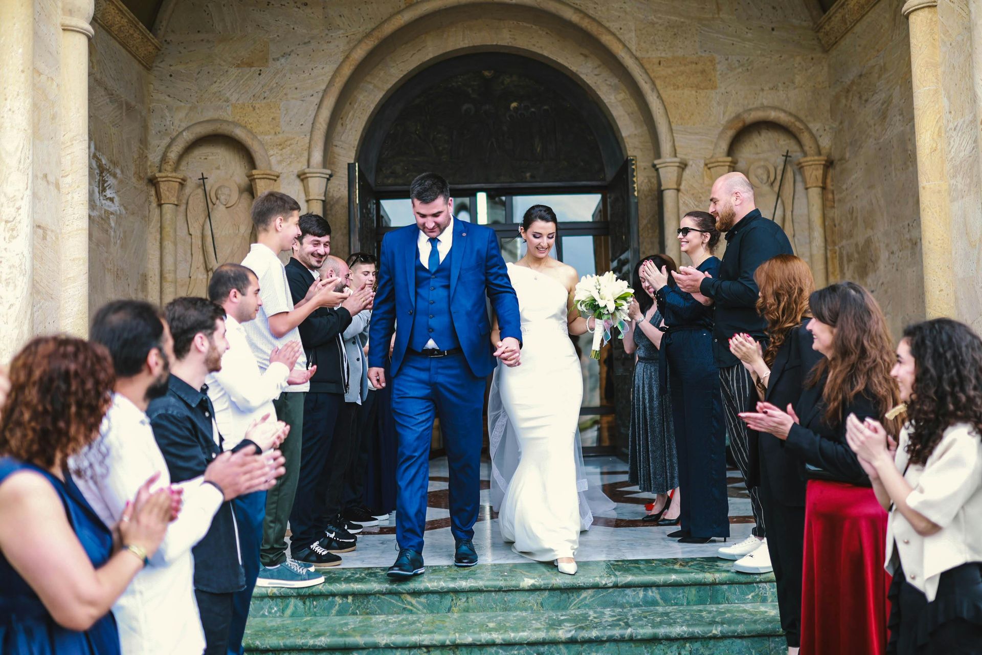 Bride and groom exit a stone church as guests applaud on either side