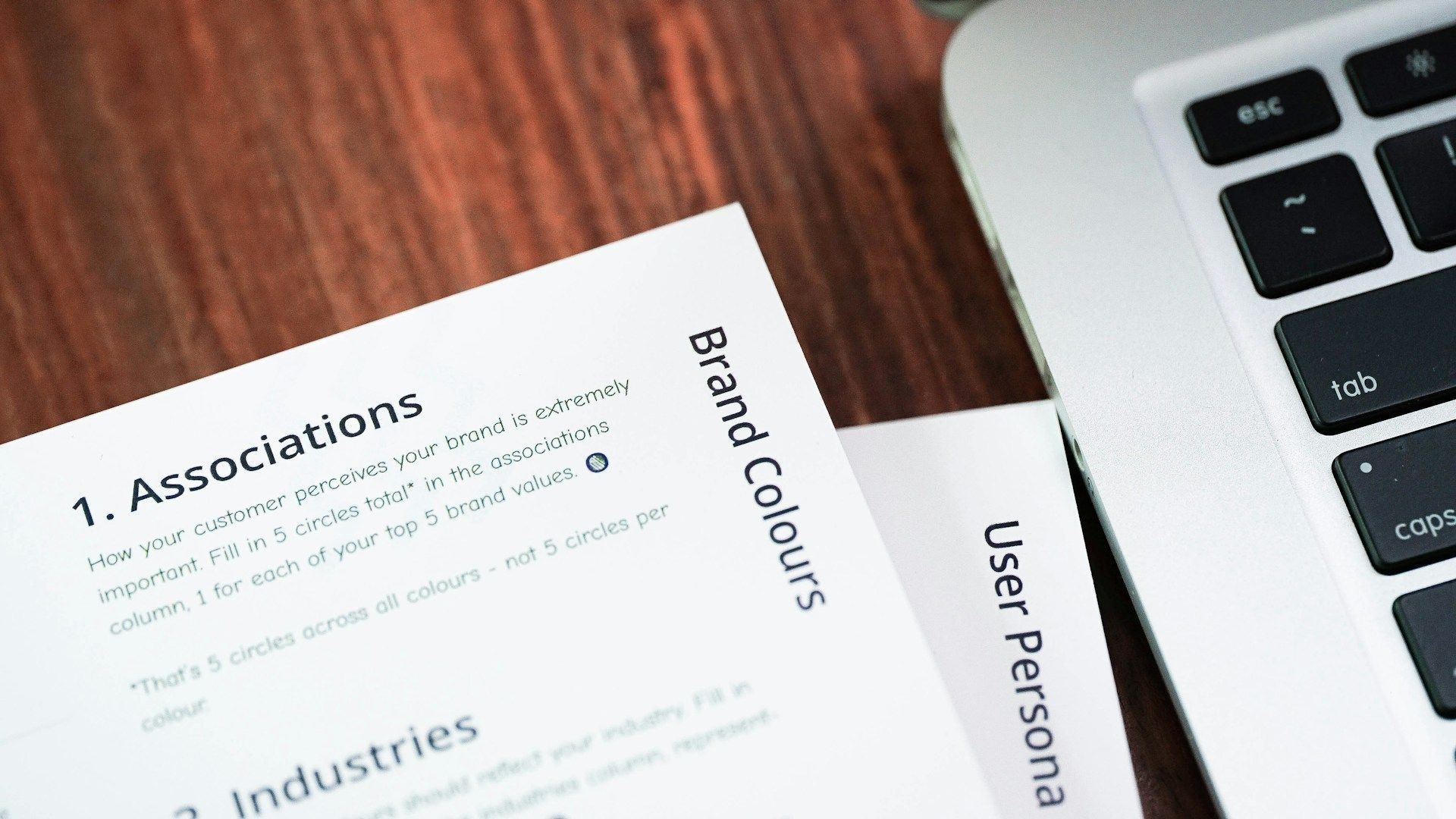 A laptop is sitting on a wooden table next to a piece of paper that says ' associations ' on it.