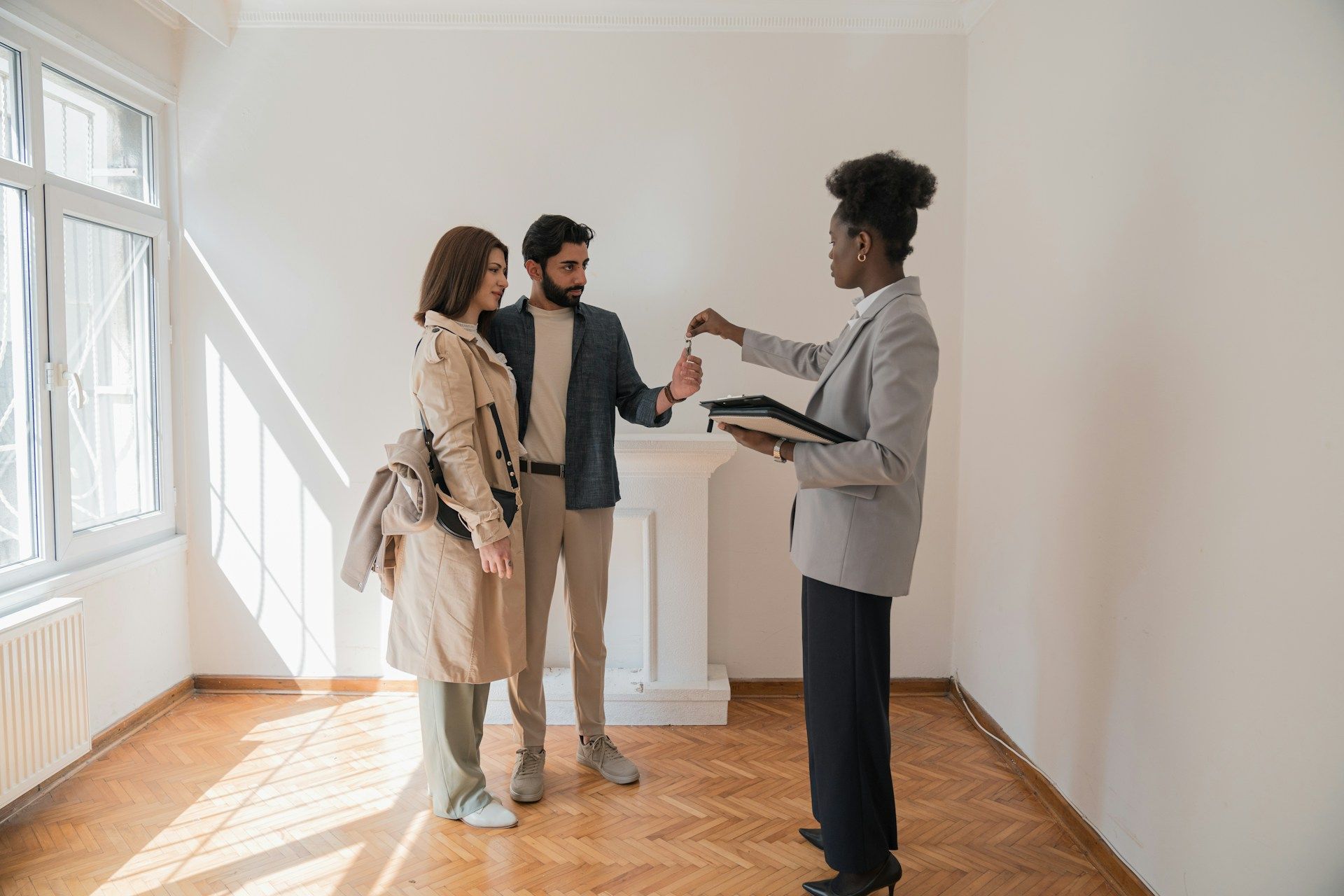 A woman is giving a key to a man and woman in an empty room.