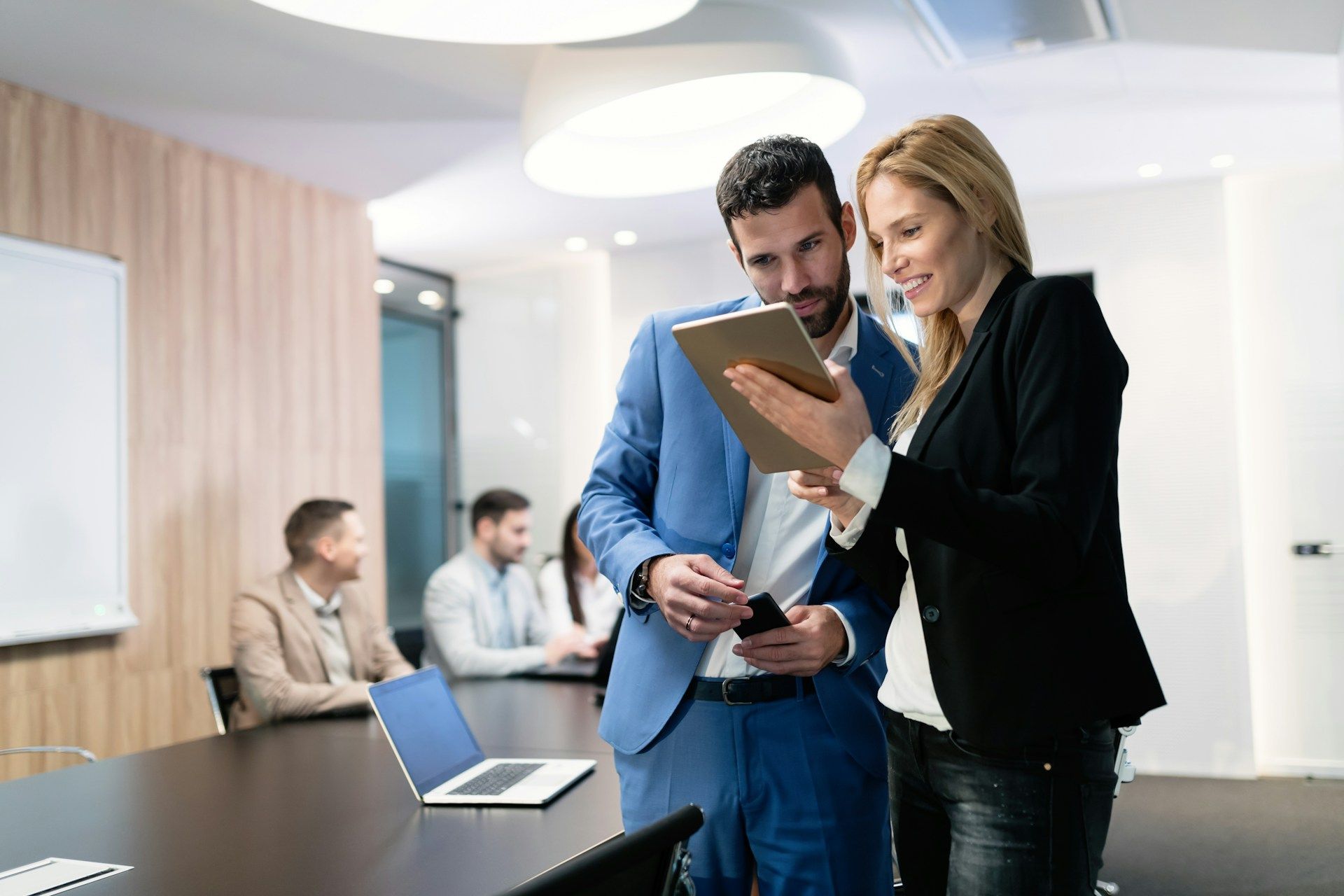 A man and a woman are looking at a tablet in a conference room.