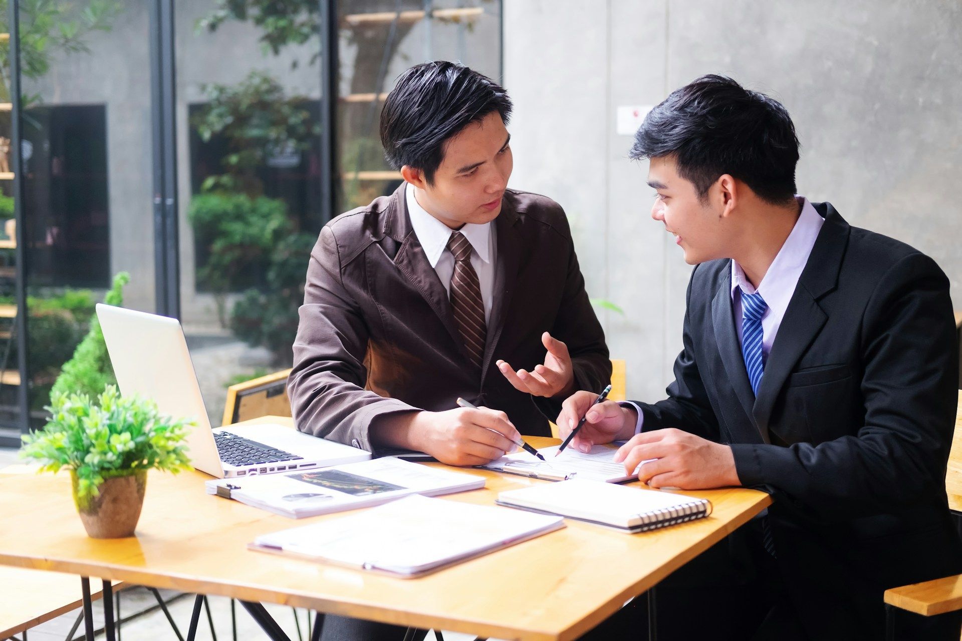 Two men in suits and ties are sitting at a table with a laptop.