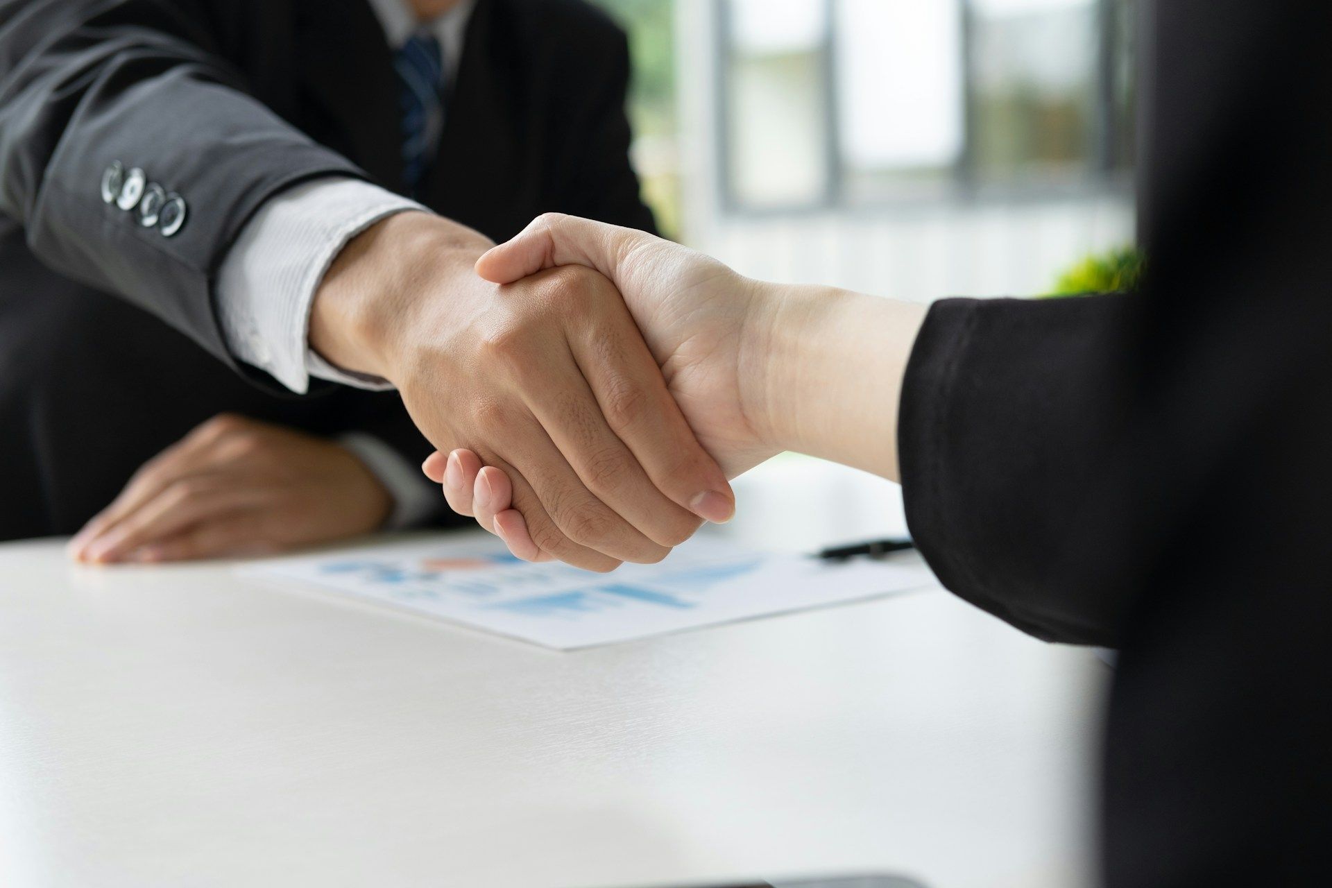 A man and a woman are shaking hands over a table.