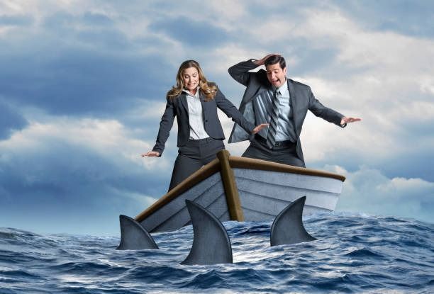 A man and a woman are in a boat surrounded by sharks.