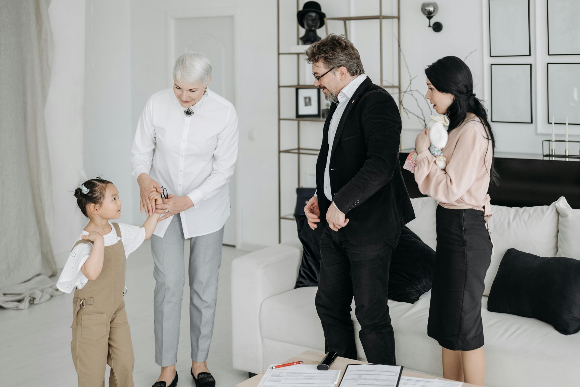 Real estate agent handing keys to a couple in an empty room with white walls, window, and a fireplace.