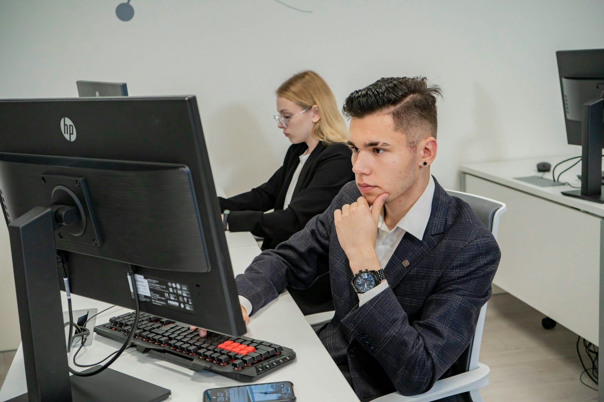 A man and a woman are sitting at a desk in front of a computer.