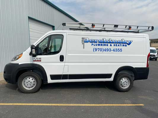 A white van with a ladder on top is parked in a parking lot.