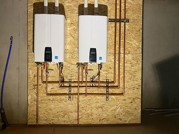 Two water heaters are hanging on a wall next to copper pipes.