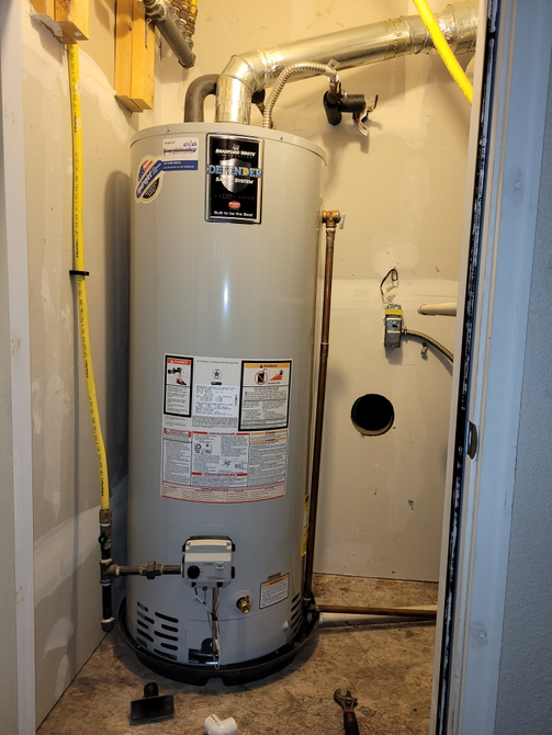 Two boilers are sitting next to each other in a room with copper pipes.