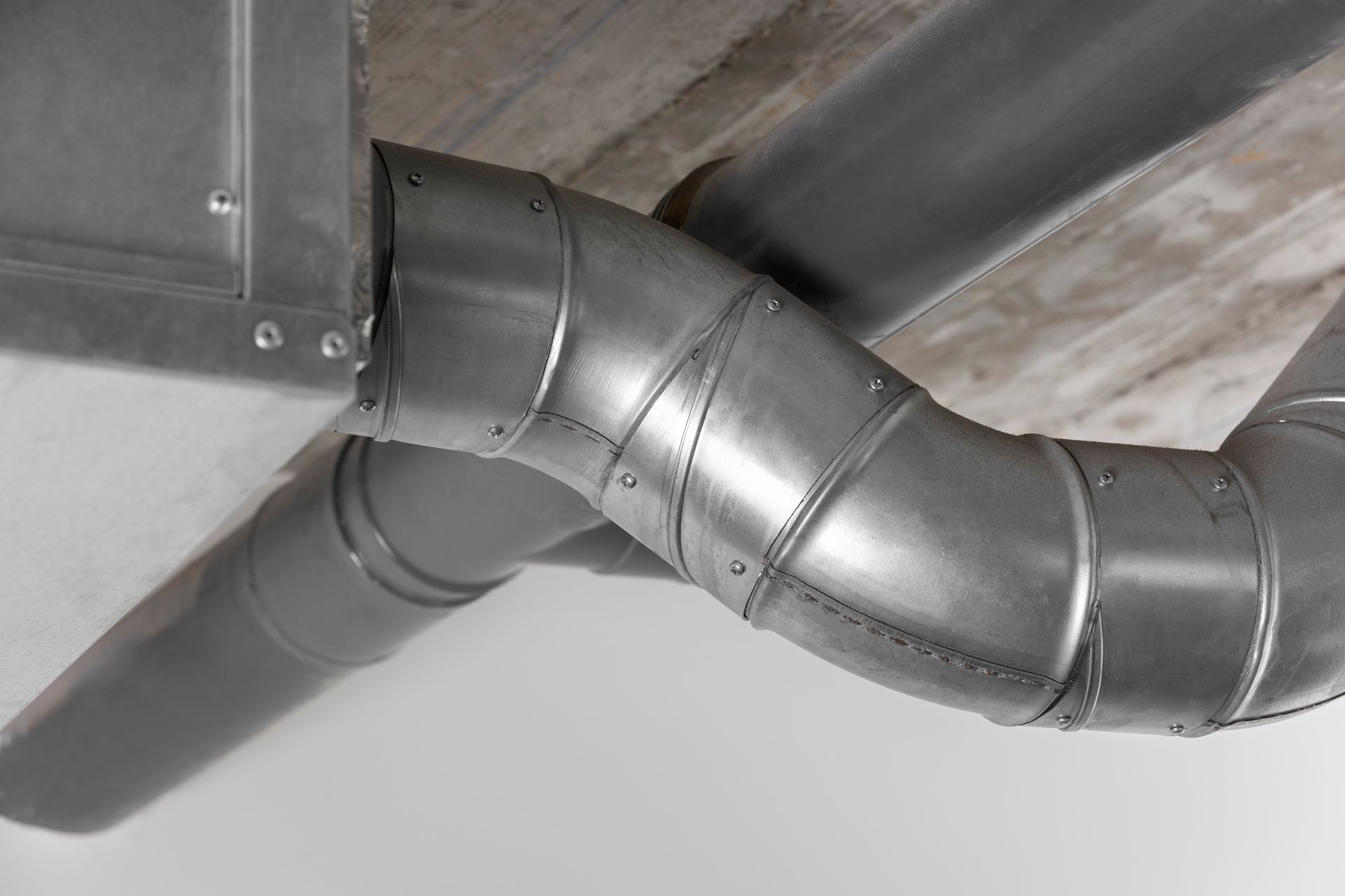 Silver HVAC ductwork bends across a white ceiling.
